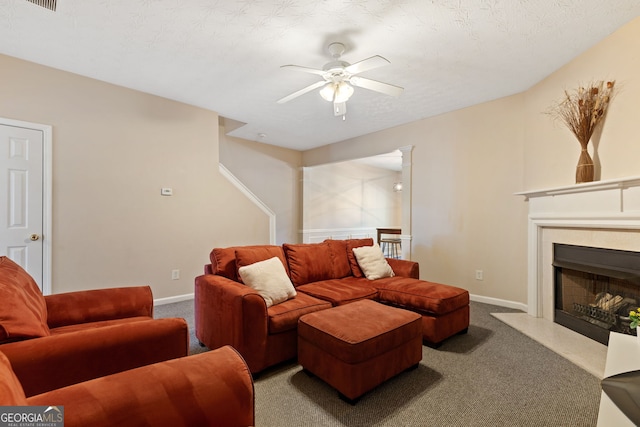 living room featuring ceiling fan, a high end fireplace, a textured ceiling, and carpet flooring