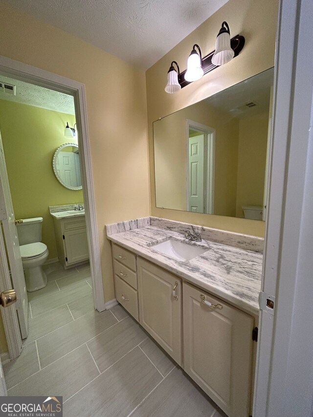 bathroom with tile patterned flooring, vanity, a textured ceiling, and toilet