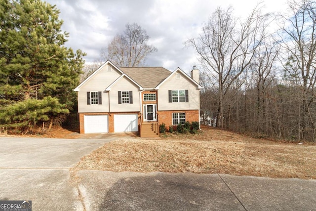 split foyer home featuring an attached garage, a chimney, concrete driveway, and brick siding