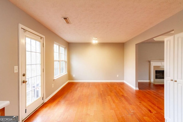 spare room featuring a textured ceiling, a fireplace with flush hearth, visible vents, baseboards, and light wood-type flooring