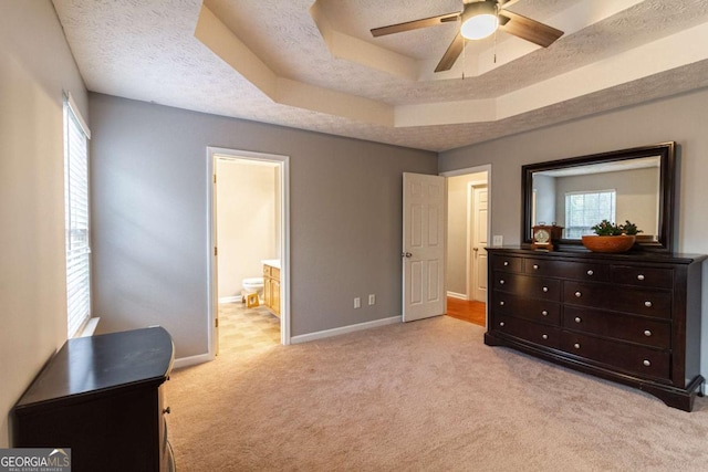 bedroom featuring light carpet, baseboards, connected bathroom, a tray ceiling, and a textured ceiling