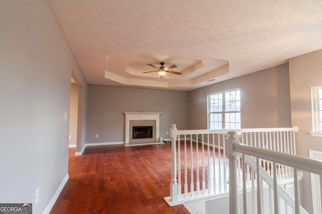 corridor with a textured ceiling, an upstairs landing, baseboards, a tray ceiling, and dark wood finished floors