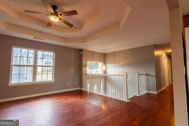 unfurnished room with baseboards, visible vents, wood finished floors, a tray ceiling, and a textured ceiling