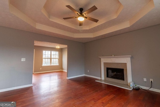 unfurnished living room featuring a raised ceiling, a premium fireplace, ceiling fan, wood finished floors, and baseboards