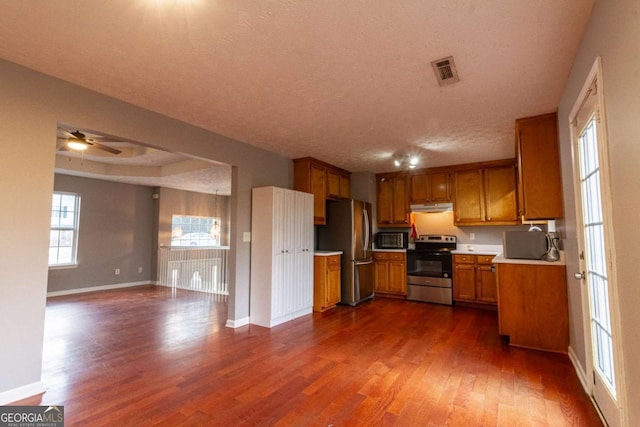 kitchen with visible vents, brown cabinets, dark wood-type flooring, stainless steel appliances, and under cabinet range hood