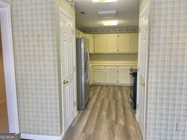 kitchen featuring hardwood / wood-style flooring, stainless steel fridge, black range with electric cooktop, and a textured ceiling