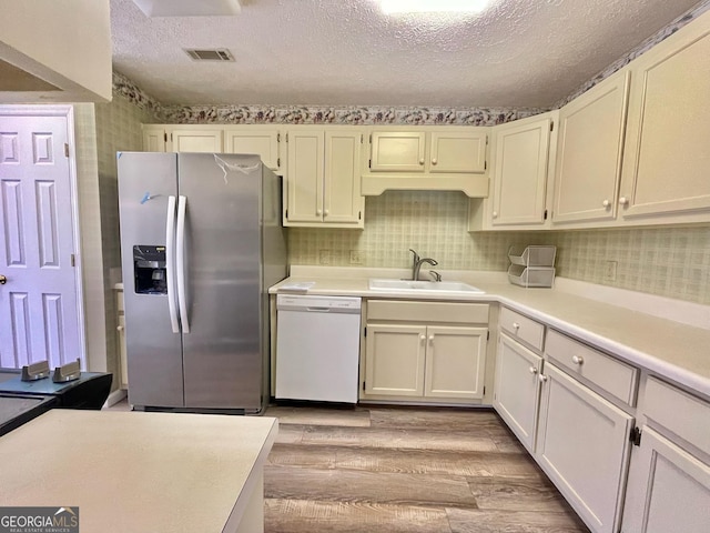 kitchen featuring sink, white dishwasher, stainless steel fridge with ice dispenser, a textured ceiling, and light hardwood / wood-style flooring