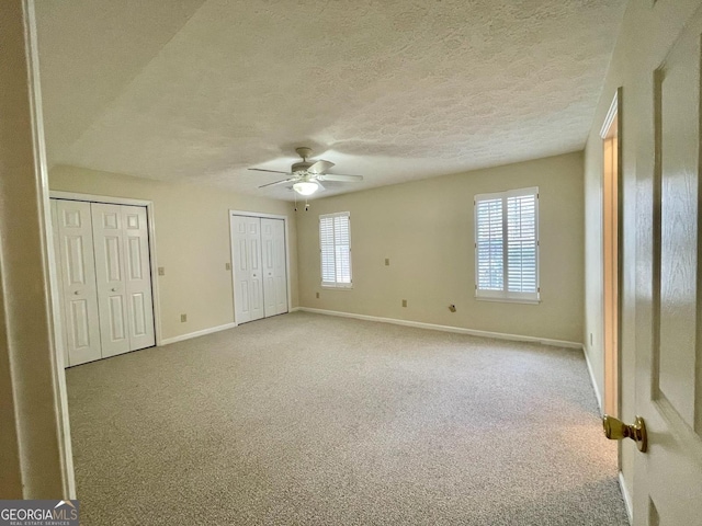 unfurnished bedroom featuring light carpet, two closets, a textured ceiling, and ceiling fan