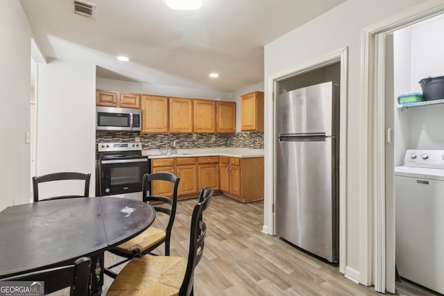 kitchen featuring tasteful backsplash, stainless steel appliances, washer / clothes dryer, and light hardwood / wood-style flooring