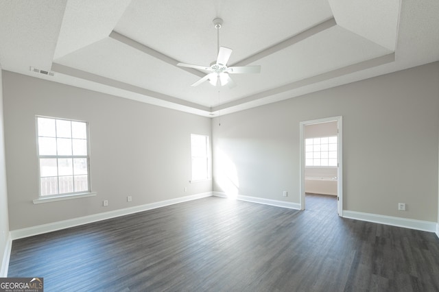 spare room featuring dark hardwood / wood-style floors, ceiling fan, plenty of natural light, and a tray ceiling