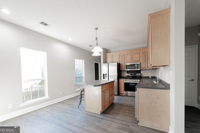 kitchen featuring pendant lighting, light brown cabinetry, a kitchen breakfast bar, a center island, and stainless steel appliances