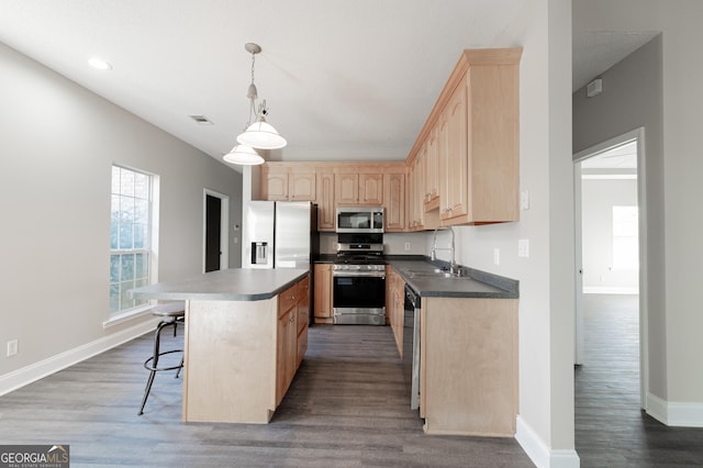 kitchen with appliances with stainless steel finishes, light brown cabinetry, sink, hanging light fixtures, and a center island