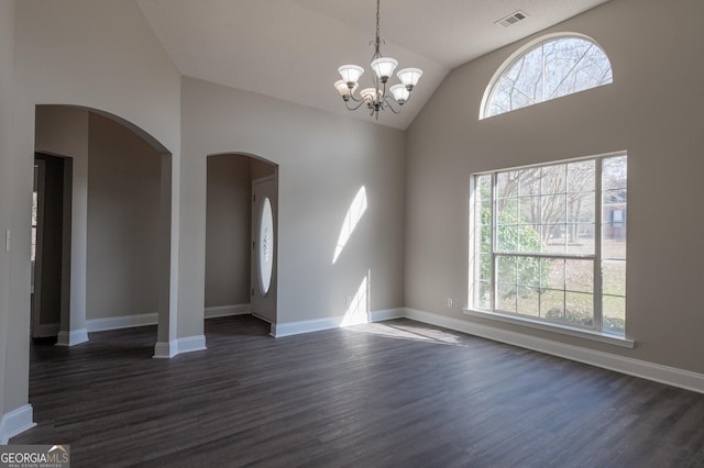 empty room featuring dark wood-type flooring, a healthy amount of sunlight, an inviting chandelier, and vaulted ceiling