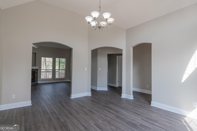 unfurnished dining area featuring a stone fireplace, dark wood-type flooring, a notable chandelier, and a towering ceiling