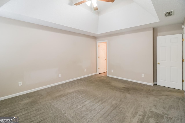 empty room with a raised ceiling, ceiling fan, and carpet