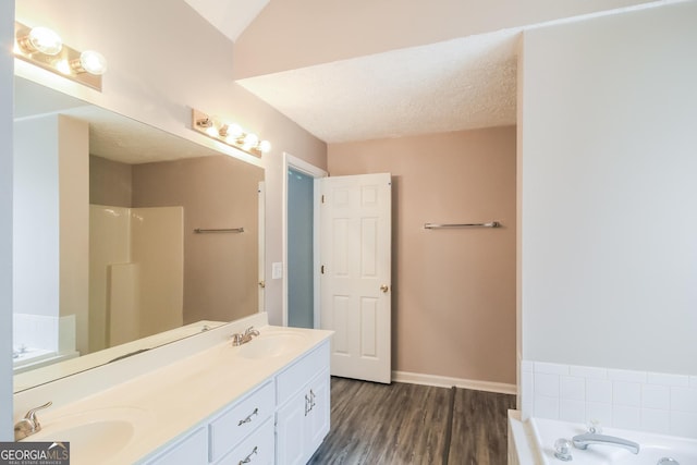 bathroom featuring hardwood / wood-style floors, lofted ceiling, a tub to relax in, vanity, and a textured ceiling