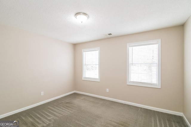 spare room with a textured ceiling, a healthy amount of sunlight, and dark colored carpet