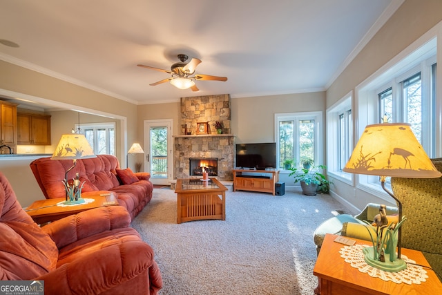 carpeted living room with crown molding, a stone fireplace, and ceiling fan