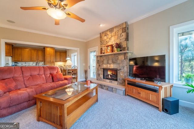 living room with crown molding, ceiling fan, a stone fireplace, and light carpet