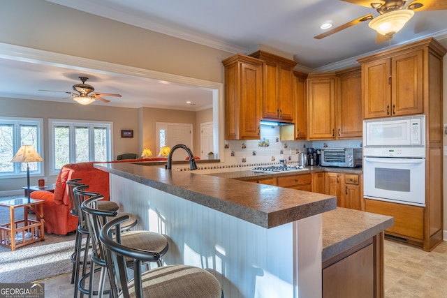 kitchen featuring a kitchen bar, decorative backsplash, kitchen peninsula, crown molding, and white appliances