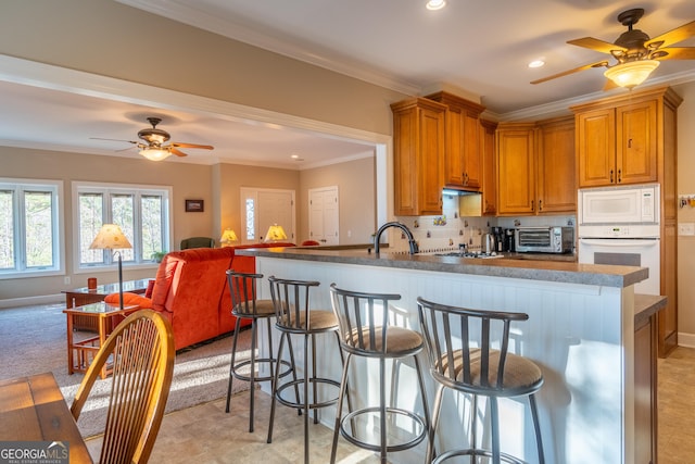 kitchen with sink, a kitchen breakfast bar, kitchen peninsula, crown molding, and white appliances