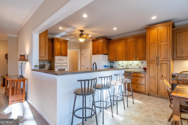 kitchen with crown molding, ceiling fan, a kitchen breakfast bar, kitchen peninsula, and white appliances