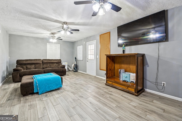 living room featuring ceiling fan, light hardwood / wood-style flooring, and a textured ceiling