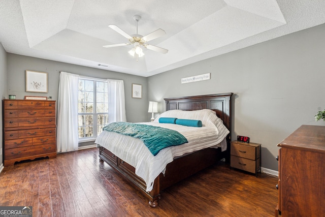 bedroom featuring ceiling fan, a tray ceiling, dark hardwood / wood-style floors, and a textured ceiling