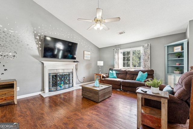 living room featuring dark wood-type flooring, vaulted ceiling, a textured ceiling, ceiling fan, and a fireplace