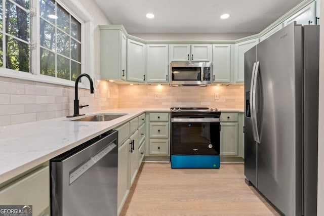 kitchen featuring sink, light stone counters, light wood-type flooring, appliances with stainless steel finishes, and backsplash