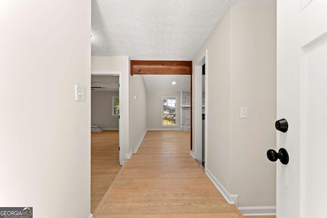 hall featuring beam ceiling, a textured ceiling, and light wood-type flooring