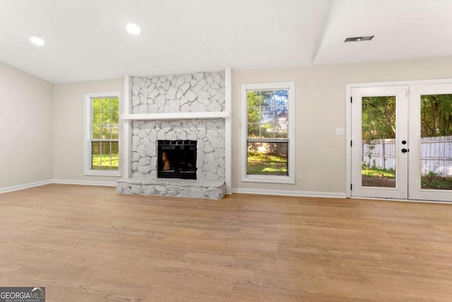 unfurnished living room with plenty of natural light, a stone fireplace, and light hardwood / wood-style flooring