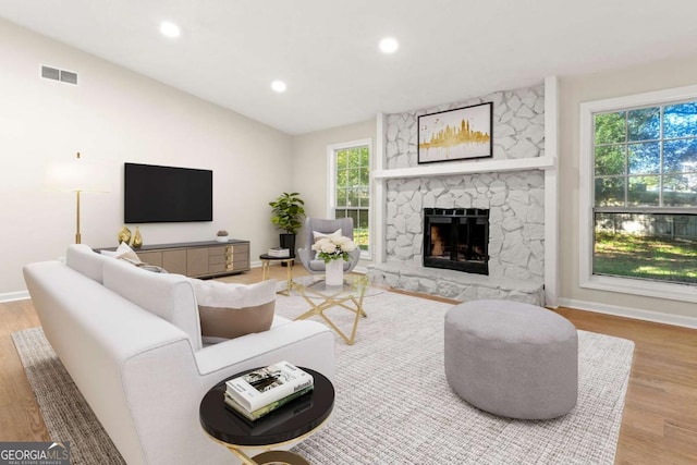 living room with lofted ceiling, a wealth of natural light, a fireplace, and light hardwood / wood-style flooring