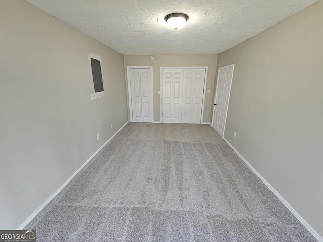 unfurnished bedroom with carpet flooring, two closets, electric panel, and a textured ceiling