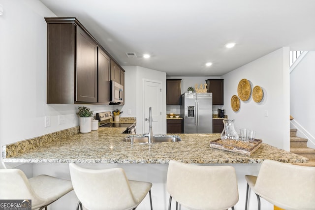 kitchen featuring appliances with stainless steel finishes, sink, light stone counters, and dark brown cabinets