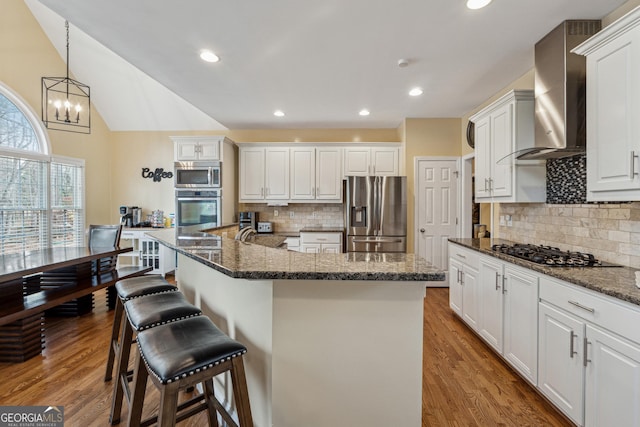 kitchen with appliances with stainless steel finishes, decorative light fixtures, tasteful backsplash, white cabinetry, and wall chimney range hood