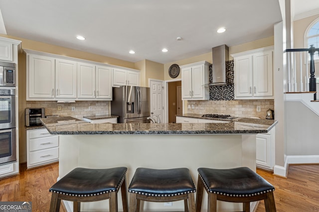 kitchen featuring a center island, wall chimney exhaust hood, white cabinets, and appliances with stainless steel finishes