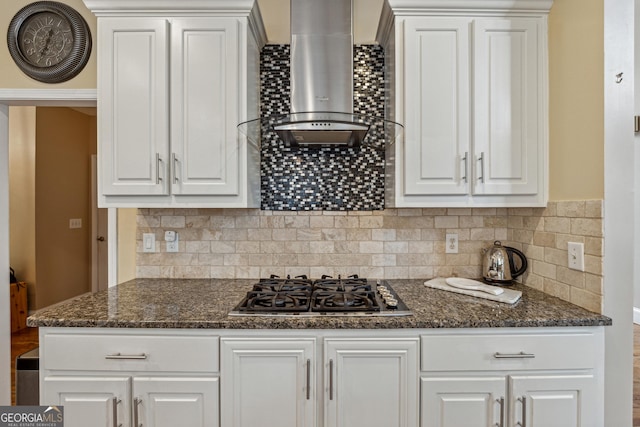 kitchen featuring white cabinetry, stainless steel gas stovetop, dark stone countertops, and wall chimney range hood