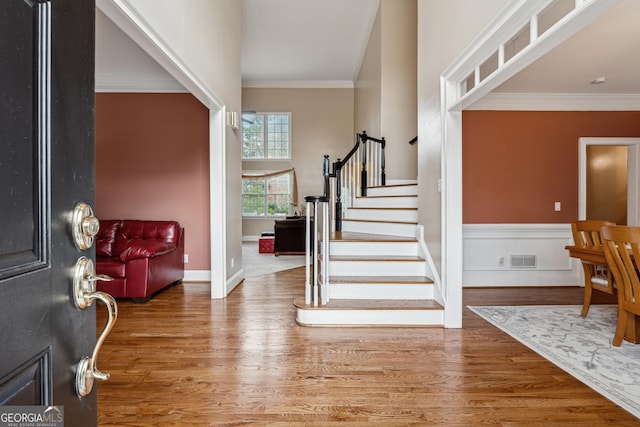 foyer featuring a towering ceiling, wood-type flooring, and ornamental molding