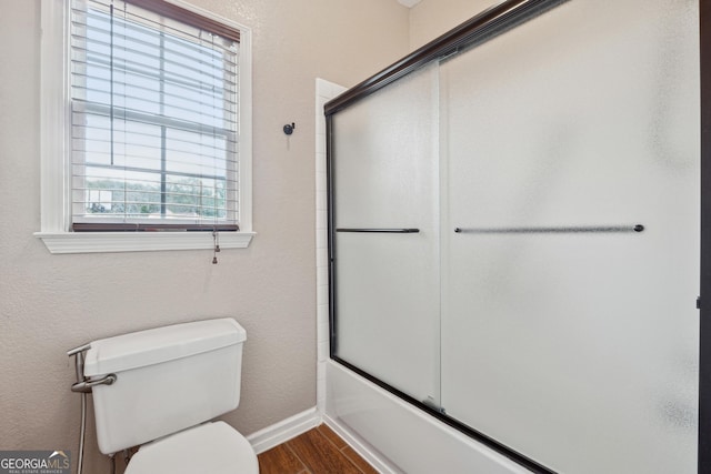 bathroom with wood-type flooring, bath / shower combo with glass door, and toilet