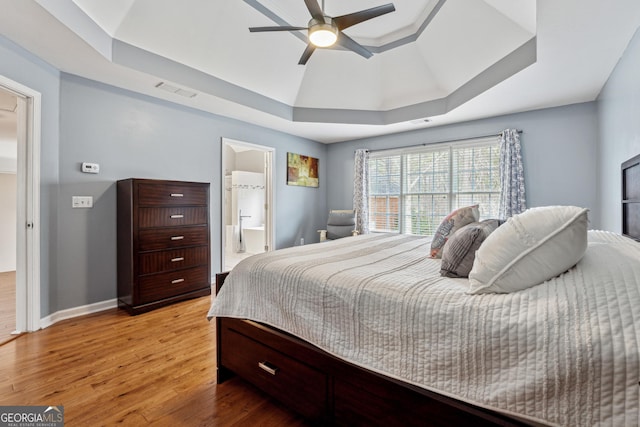 bedroom featuring ensuite bathroom, light hardwood / wood-style flooring, ceiling fan, and a tray ceiling