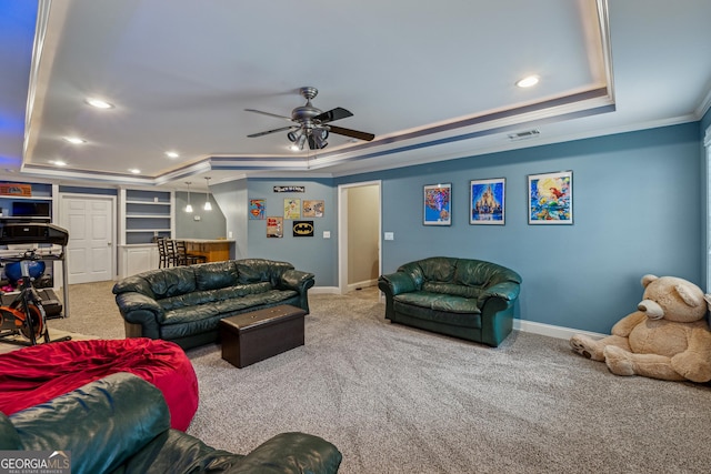 living room featuring ornamental molding, a raised ceiling, carpet floors, built in features, and ceiling fan