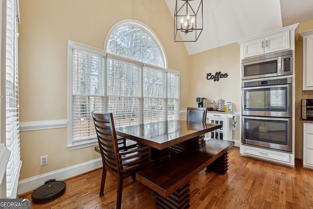 dining area featuring a healthy amount of sunlight, high vaulted ceiling, hardwood / wood-style floors, and a notable chandelier