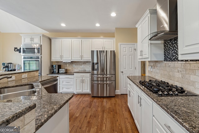 kitchen featuring white cabinetry, sink, dark stone counters, stainless steel appliances, and wall chimney range hood