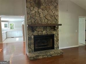 unfurnished living room featuring a stone fireplace, vaulted ceiling, and hardwood / wood-style flooring