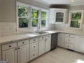 kitchen with tasteful backsplash, white cabinetry, dishwasher, sink, and light stone countertops