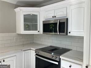 kitchen with tasteful backsplash, ornamental molding, appliances with stainless steel finishes, and white cabinets