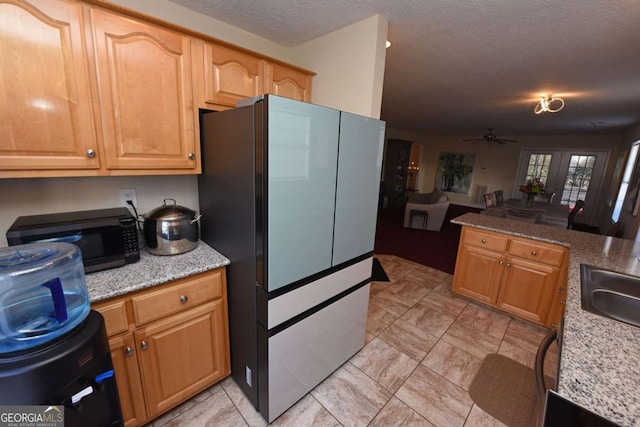 kitchen with stainless steel refrigerator, ceiling fan, light stone countertops, and a textured ceiling