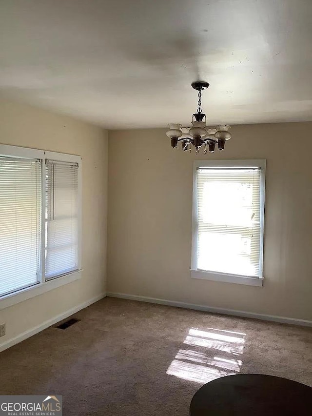 carpeted empty room with an inviting chandelier