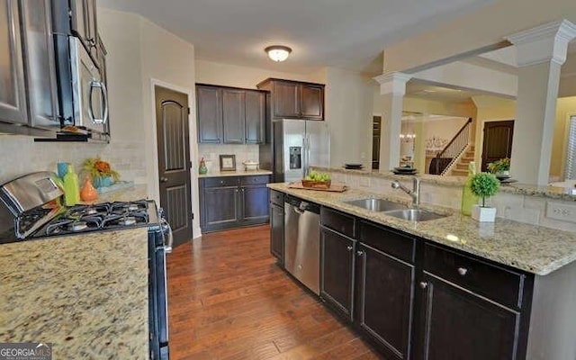 kitchen with sink, tasteful backsplash, stainless steel appliances, light stone countertops, and decorative columns